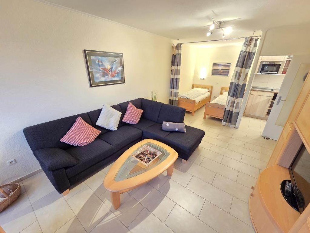 Wohnbereich mit Sofa, Couchtisch und Blick in Schlafzimmer mit zwei Betten.