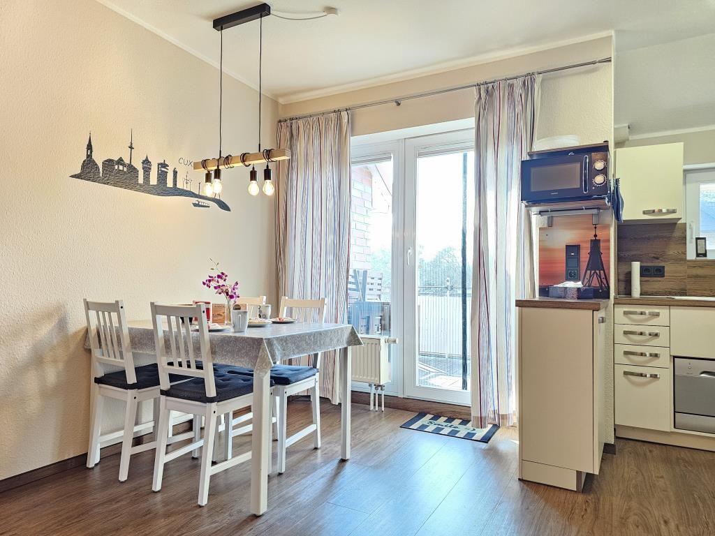 Esszimmer mit Tisch, Stühlen und Blick auf Balkon. Küche mit Mikrowelle und Arbeitsplatte.