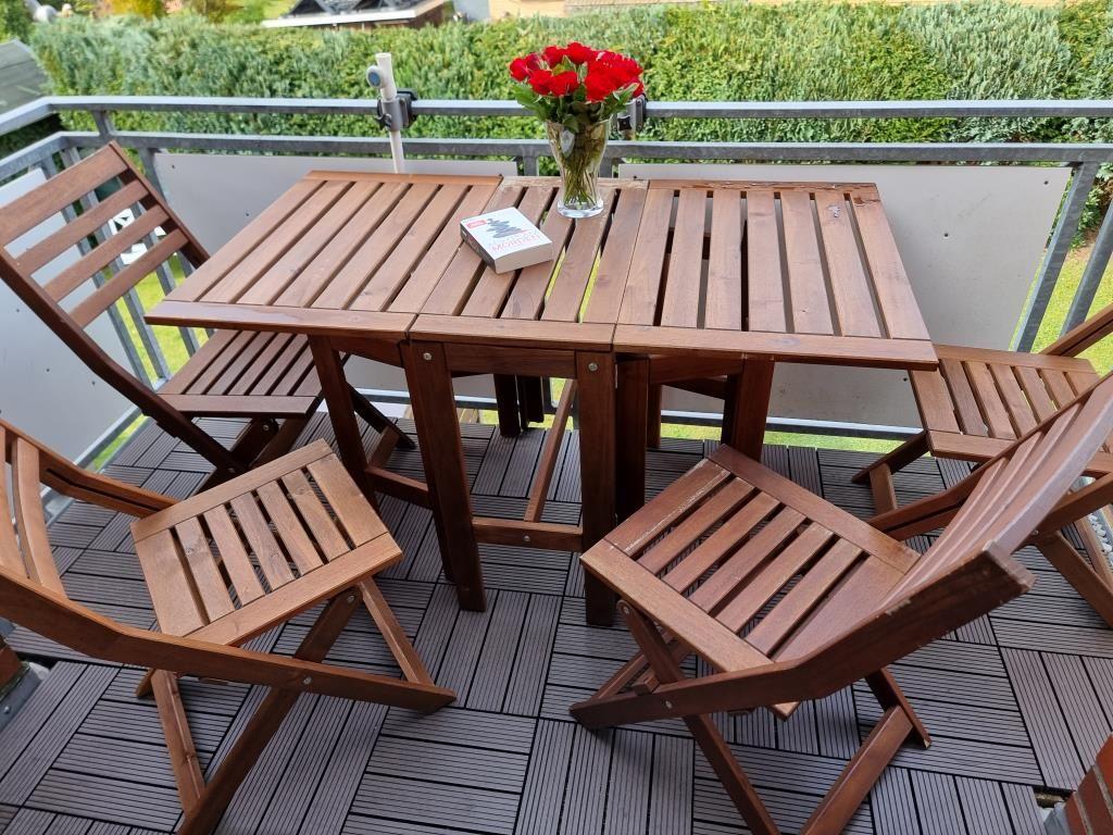 Terrasse mit Holztisch und Stühlen, Blumen und Buch. Blick auf grünen Garten.