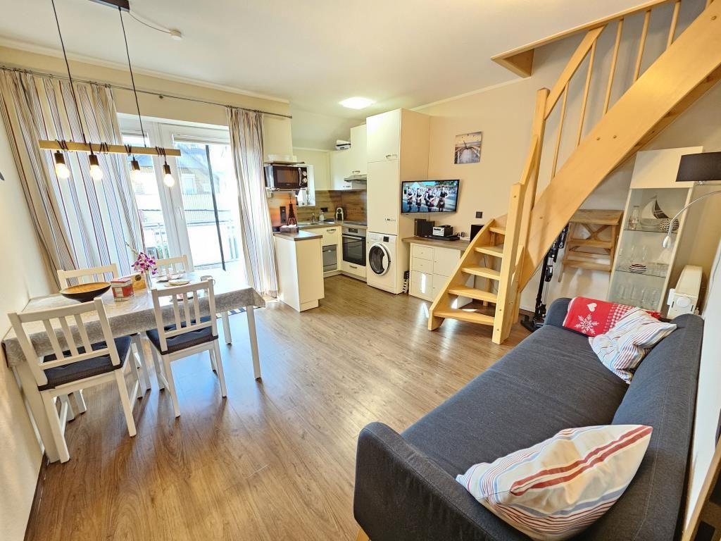 Wohnung mit Essbereich, Küche und Sofa. Holztreppe führt zur oberen Etage.