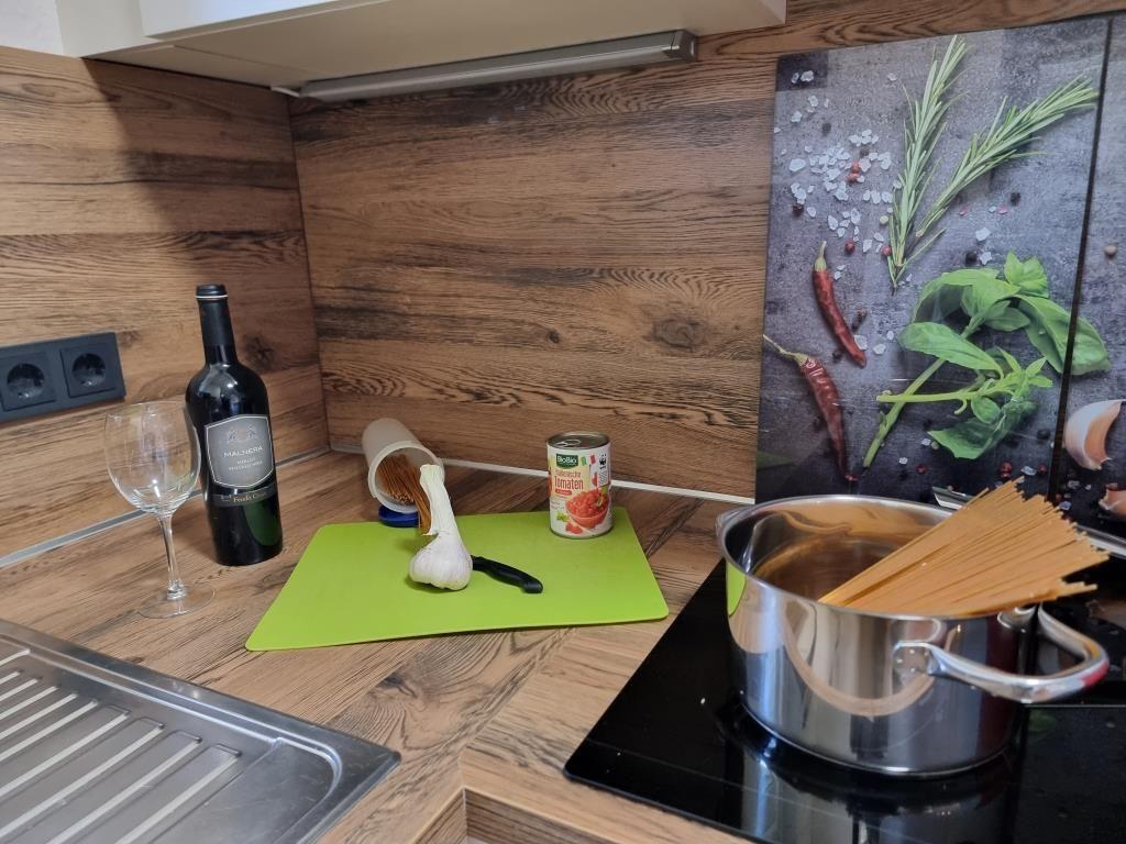 Küche mit Kochtopf, Spaghetti, Knoblauch und Wein auf Holzoberfläche.