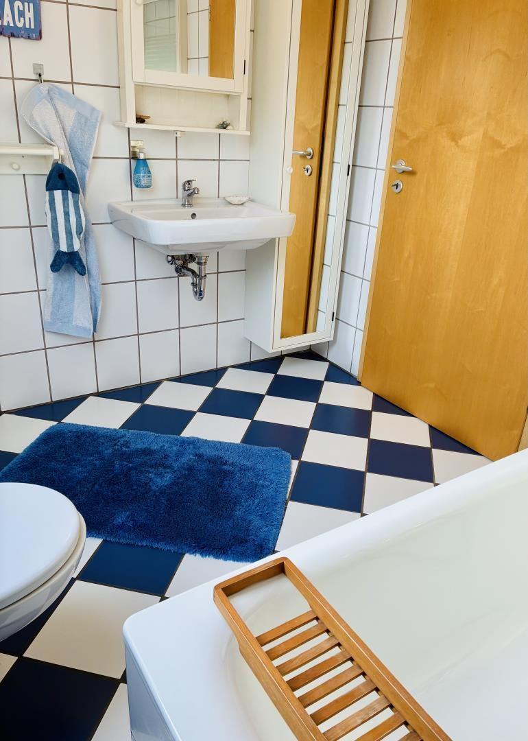 Badezimmer mit blau-weißem Fliesenboden, Waschbecken, Toilette und Badewanne.