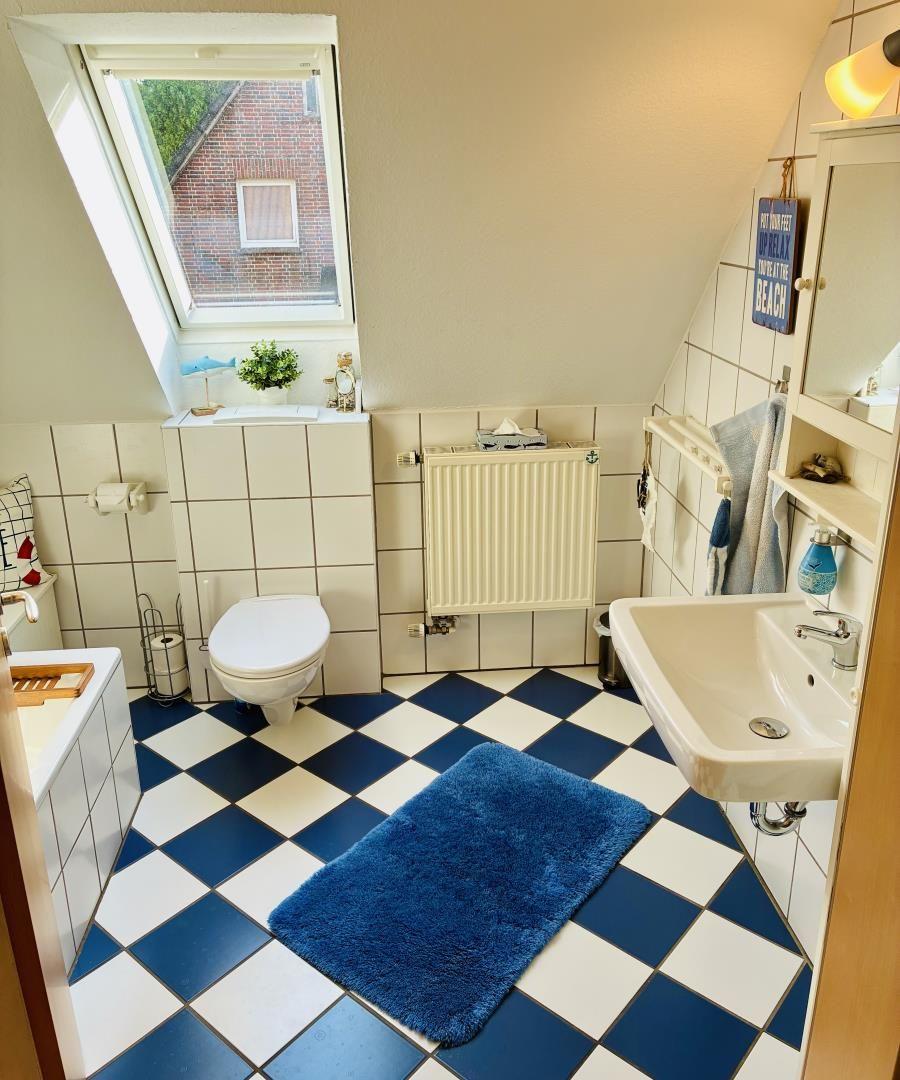 Badezimmer mit Dachfenster, Toilette, Waschbecken und blau-weißem Fliesenboden.
