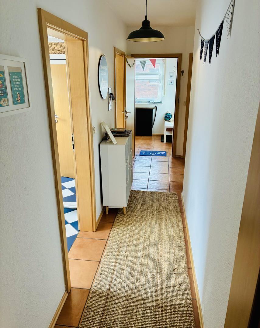 Flur mit Teppich, Tür zu Schlafzimmer und Küche, Wanddekoration und Hängelampe.