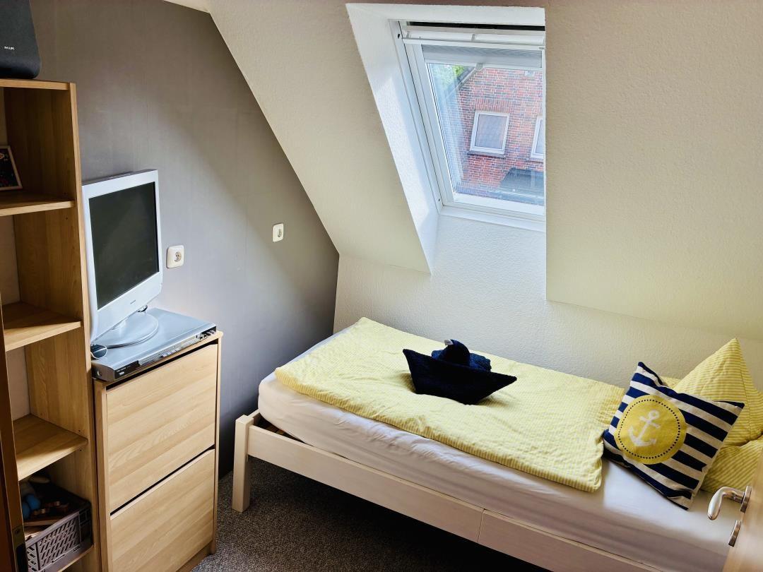 Schlafzimmer mit Dachschrägen, Bett, TV und Fenster.