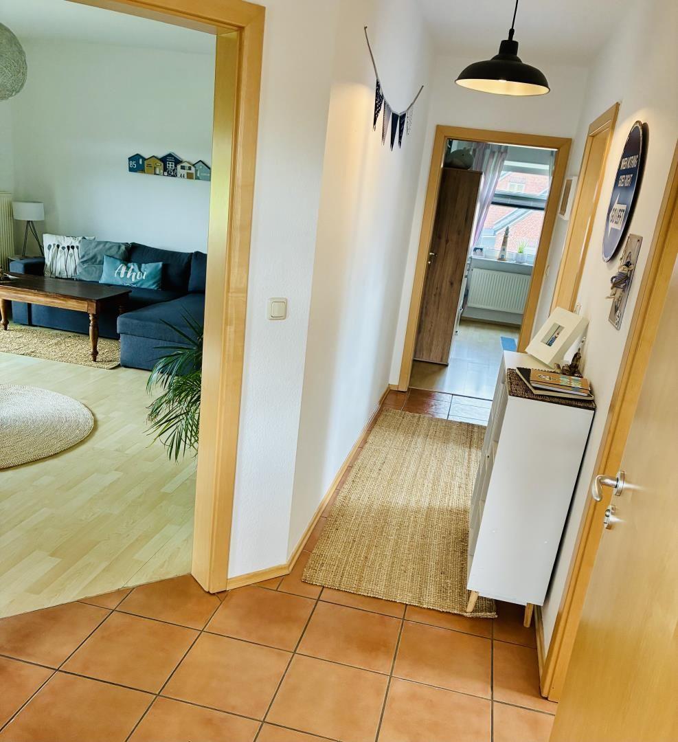 Flur mit Teppich, weißen Schrank und Tür zum Wohnzimmer mit Sofa und Couchtisch.