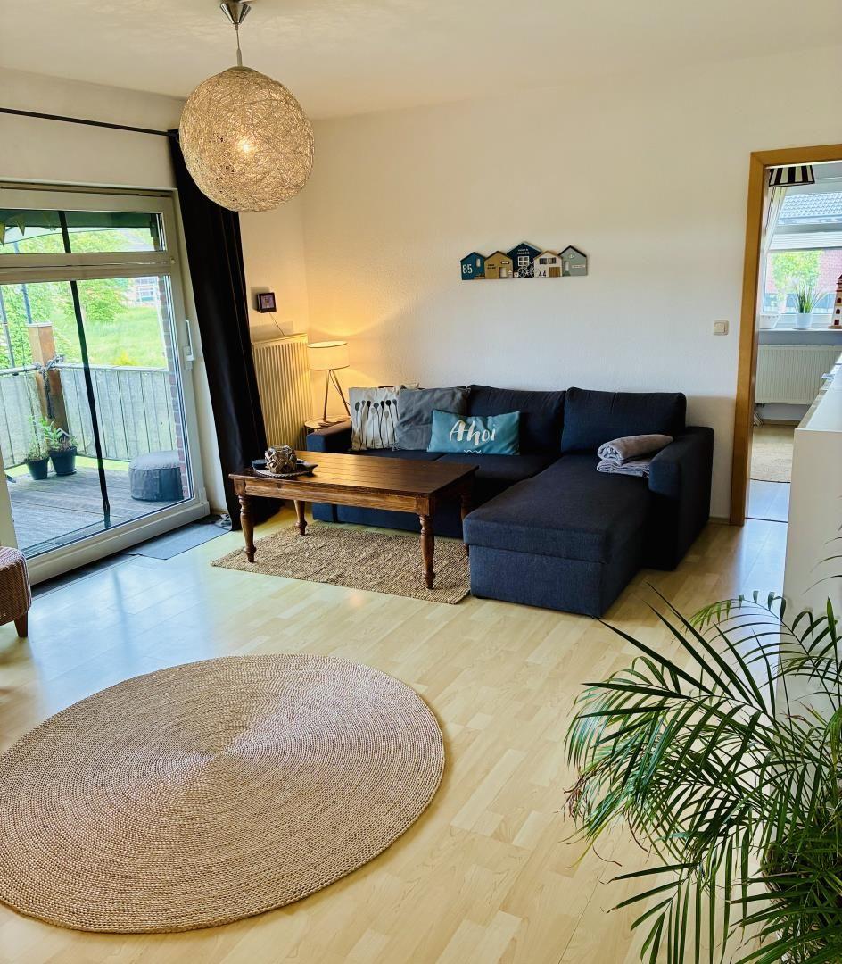 Wohnzimmer mit Sofa, Holztisch und runden Teppich. Durchgang zur Küche. Terrasse über Glastür.