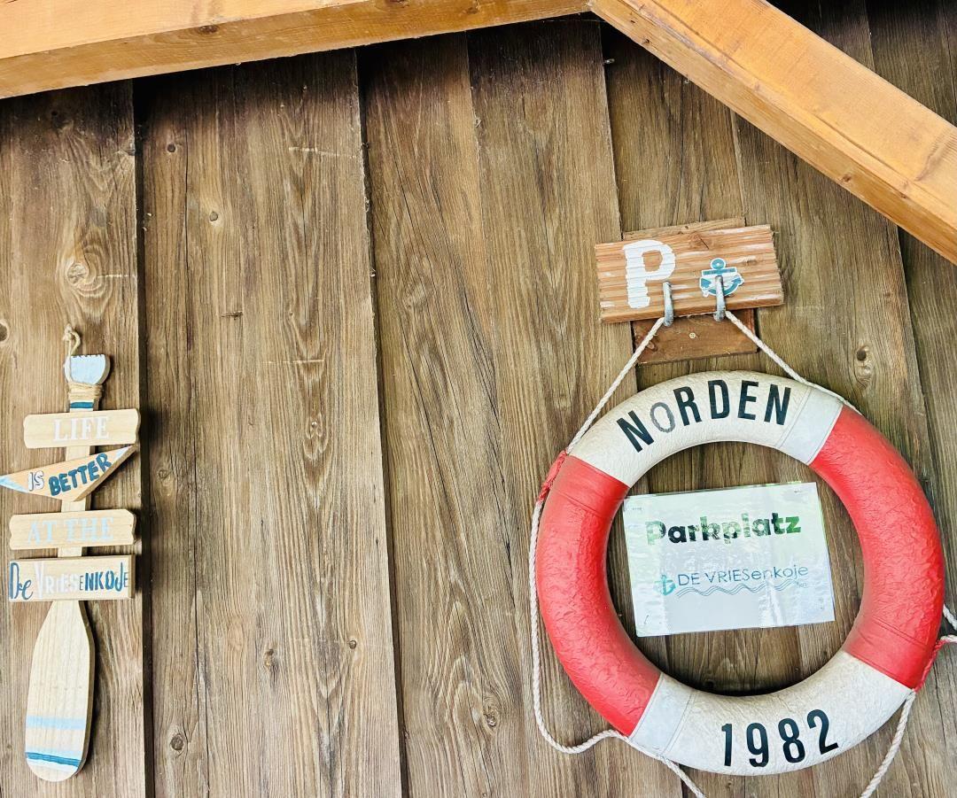 Rettungsring mit Parkplatzschild an Holzwand. Holzschild mit Segelschiffmotiv.