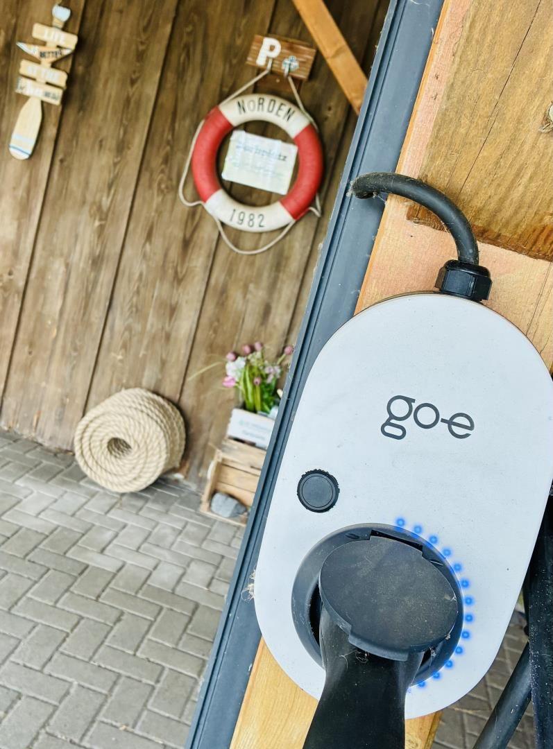 Ladestation für Elektrofahrzeuge an einer Holzwand mit Rettungsring und Seilrolle.