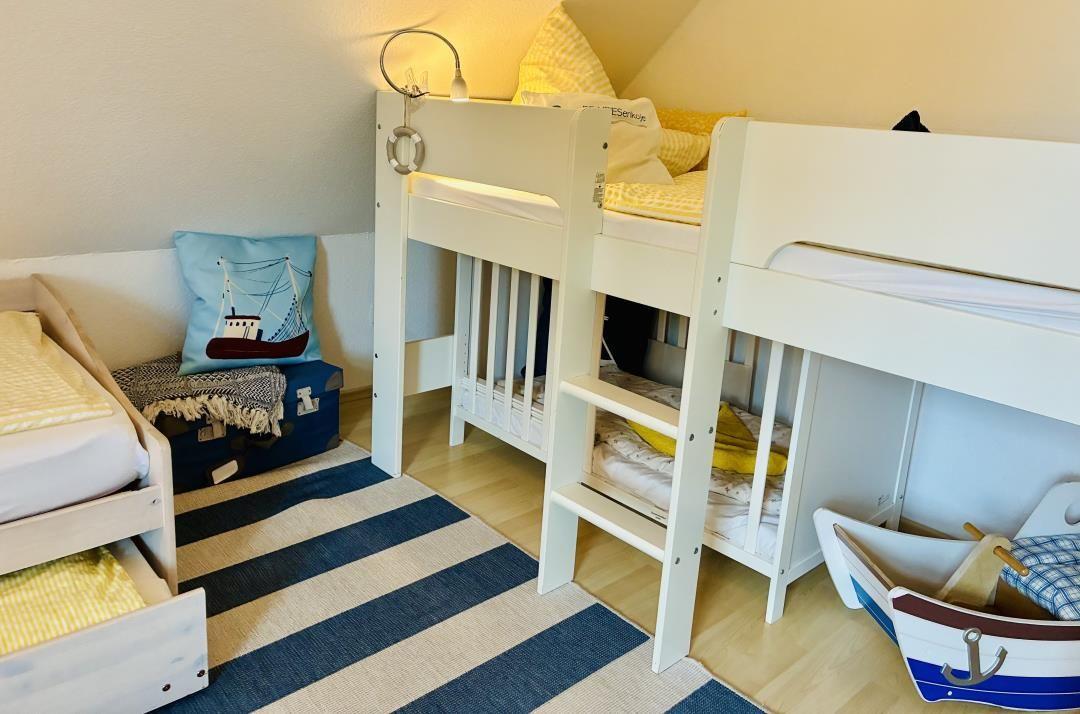 Zimmer mit Doppelstockbett, Matratze, Kissen und blau-weißem Teppich.