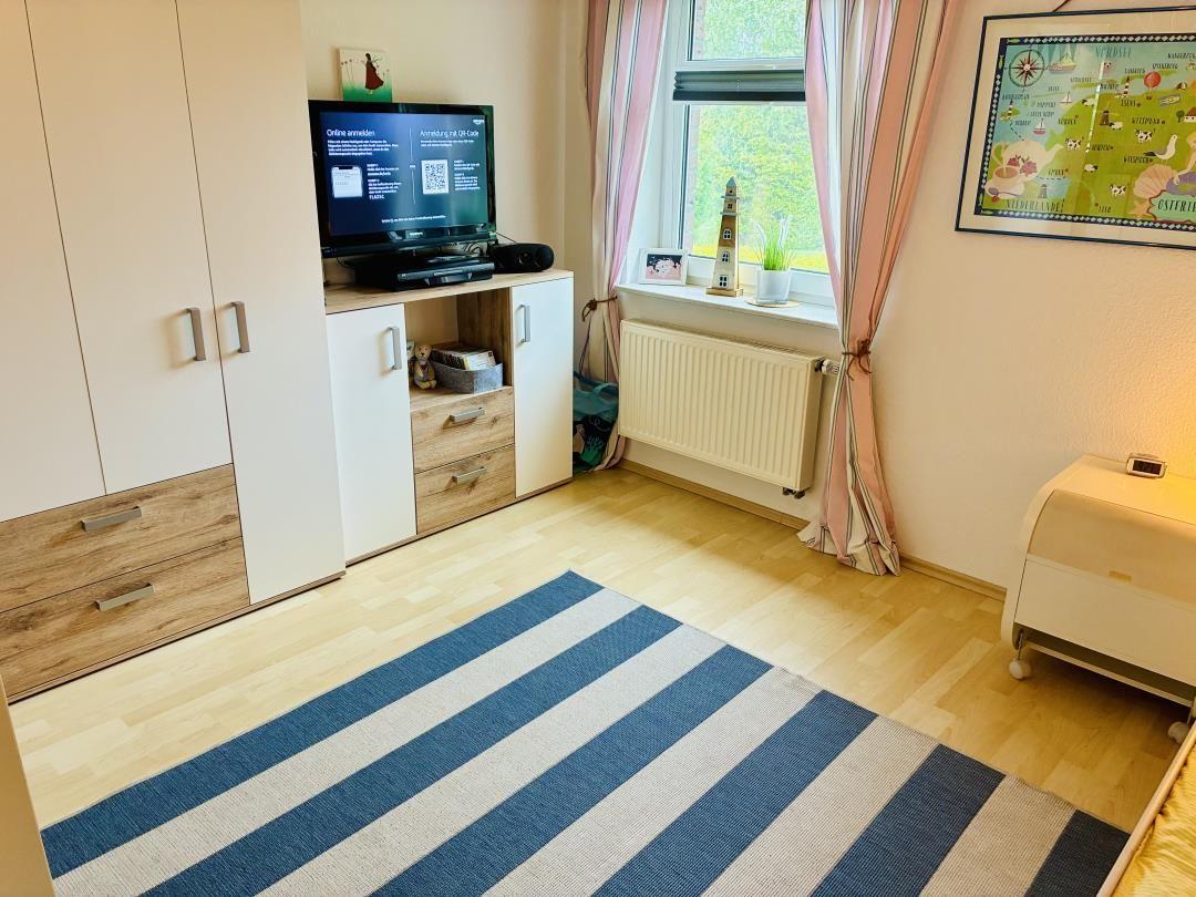 Schlafzimmer mit TV, Schrank und Fenster mit Blick auf Grün.