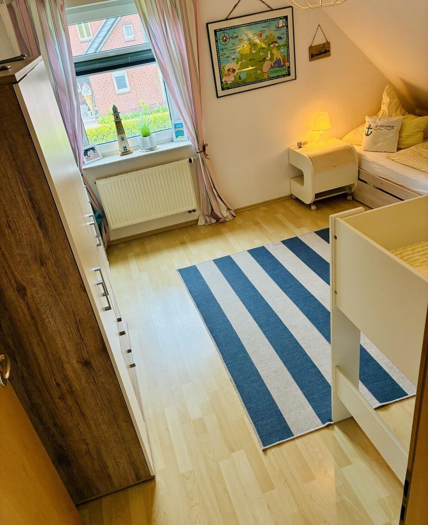 Schlafzimmer mit Kinderbett, Bett, Kleiderschrank und Fenster mit Blick auf Außenbereich.