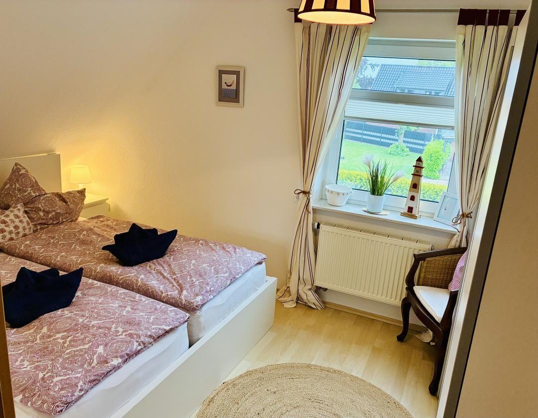 Schlafzimmer mit Doppelbett, Fenster, Vorhang und Sitzgelegenheit.