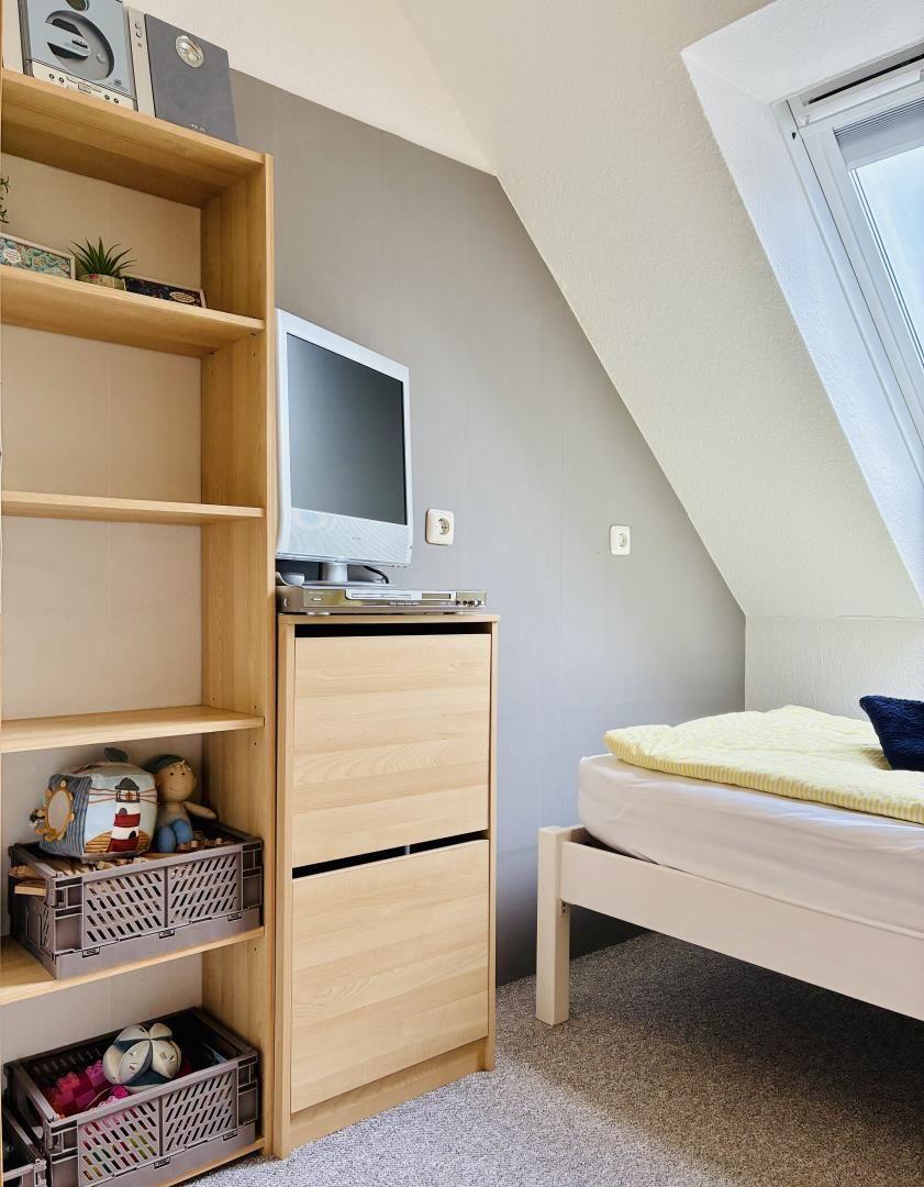 Schlafzimmer mit Bett, TV und Bücherregal unter Dachschrägen.