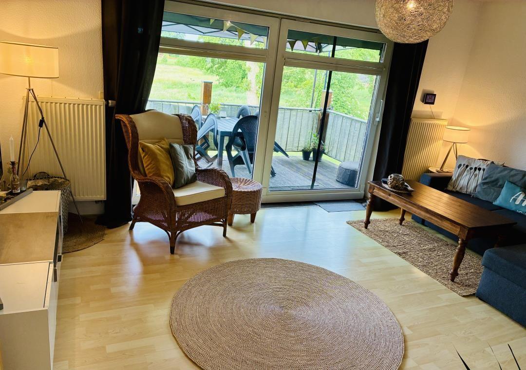 Wohnzimmer mit Sitzgelegenheiten und Balkonzugang. Holzboden und runder Teppich.