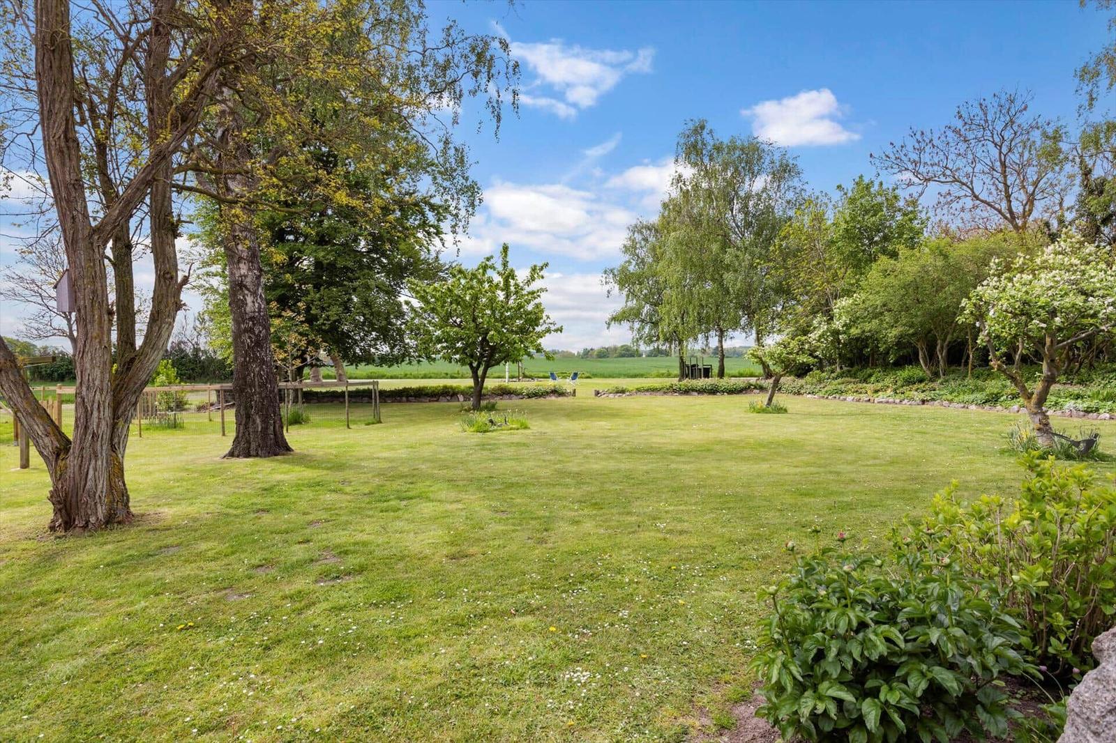 Large green garden with trees and view of fields under blue sky.