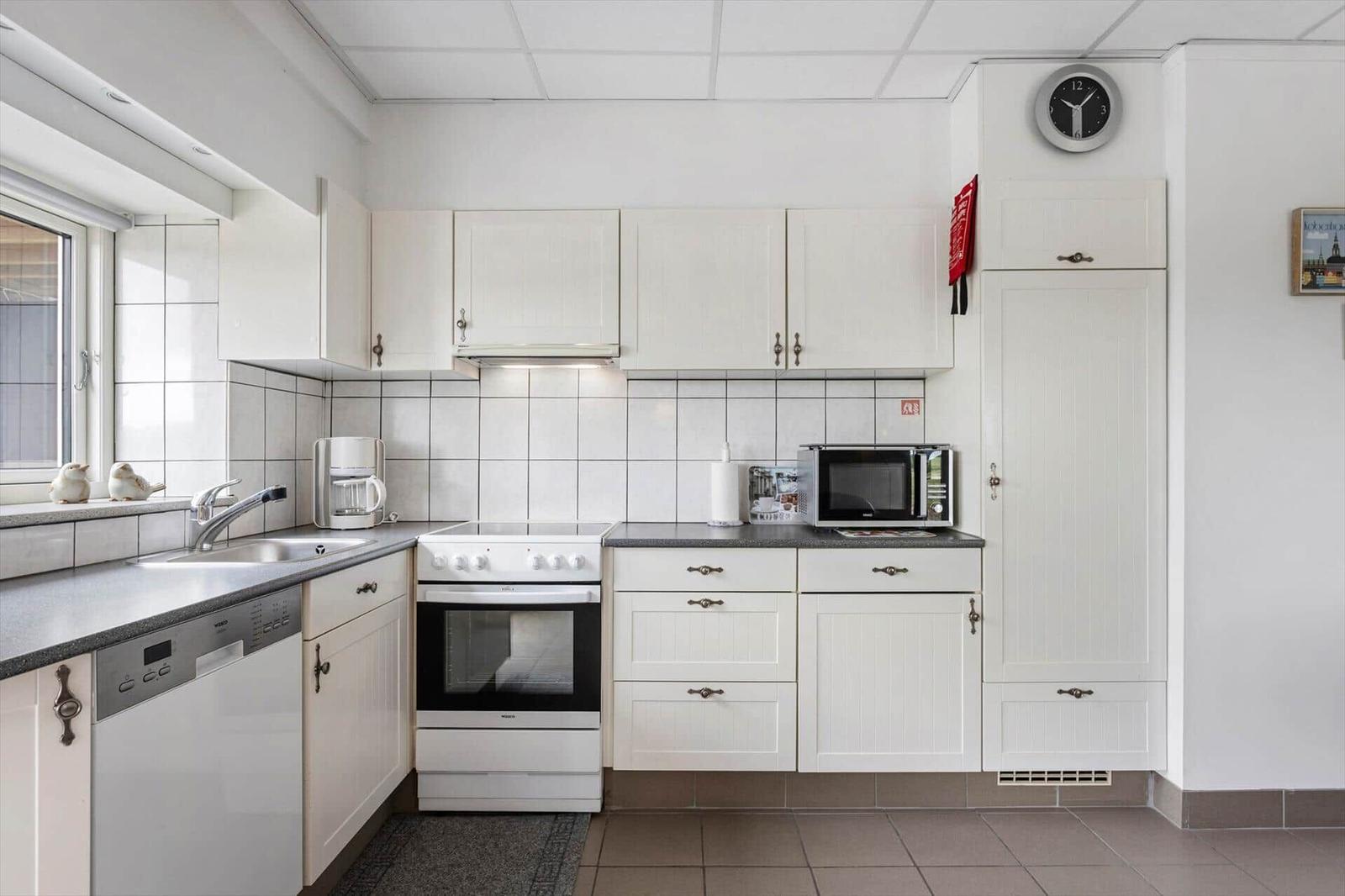 Kitchen with white cabinets, sink, stove, and microwave. Window with bird figurines.