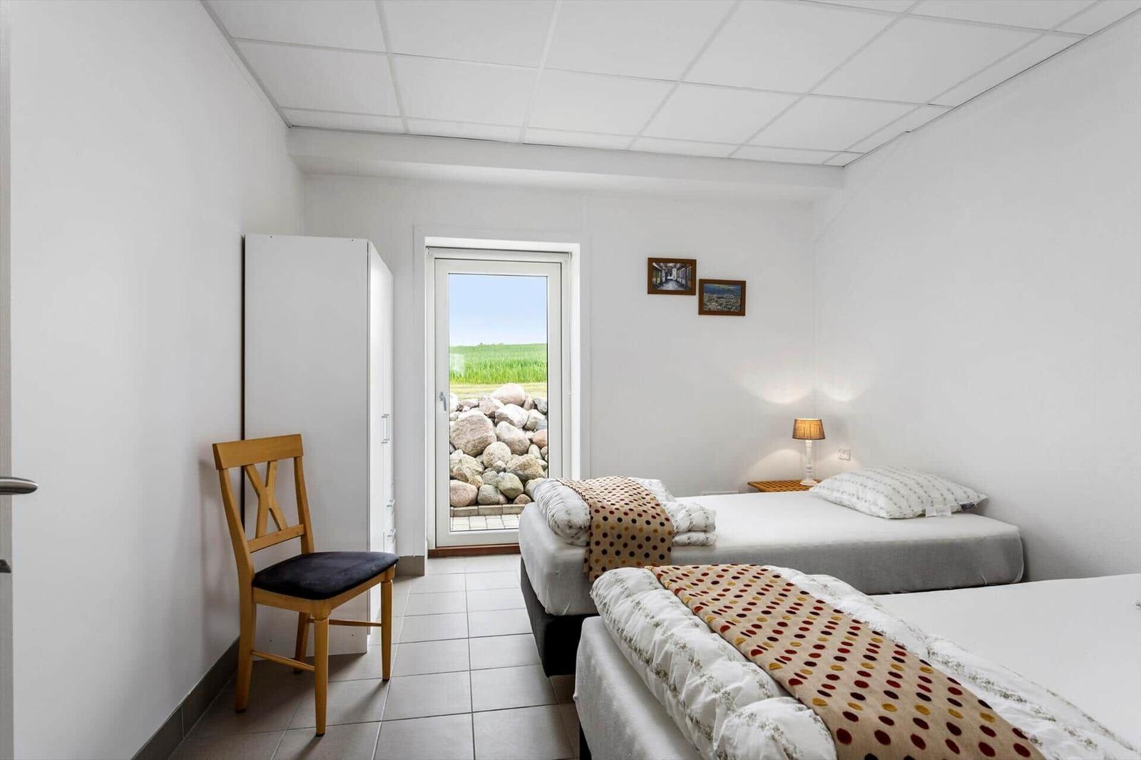 Two beds, chair, wardrobe, and door with view of grass and stones.