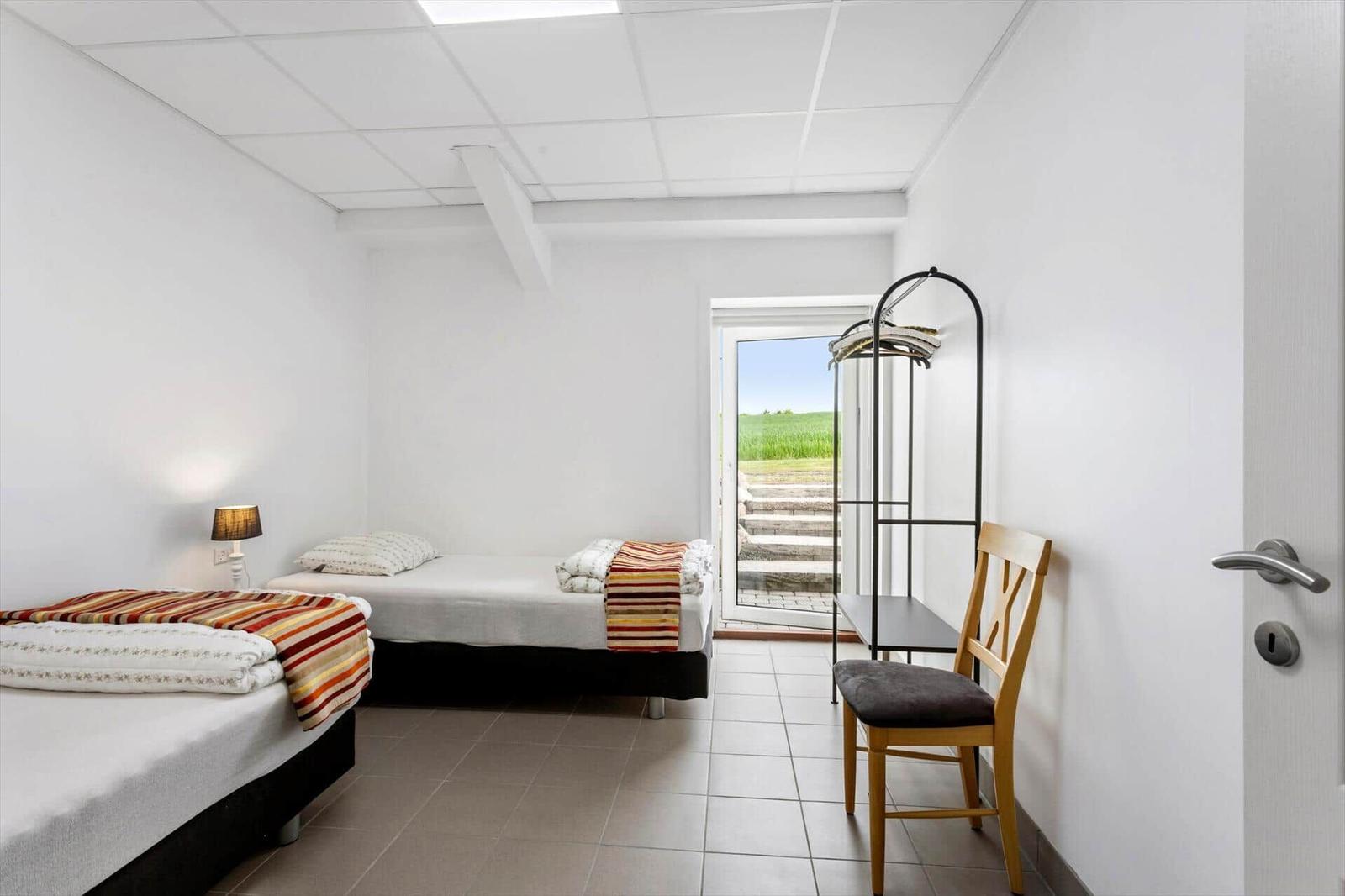 Two single beds, chair, coat rack, and door with view of green area.