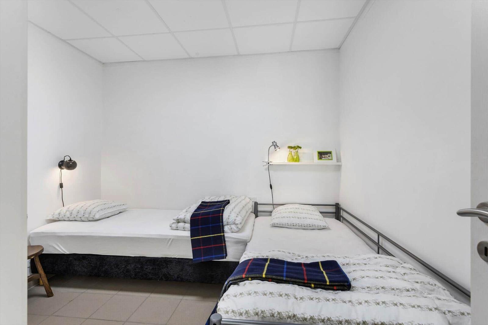 Two single beds with bedding and blankets in a room with white walls and ceiling.