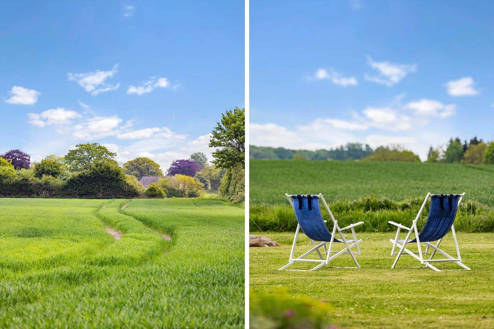 Two blue lounge chairs sit on a green lawn under a blue sky.