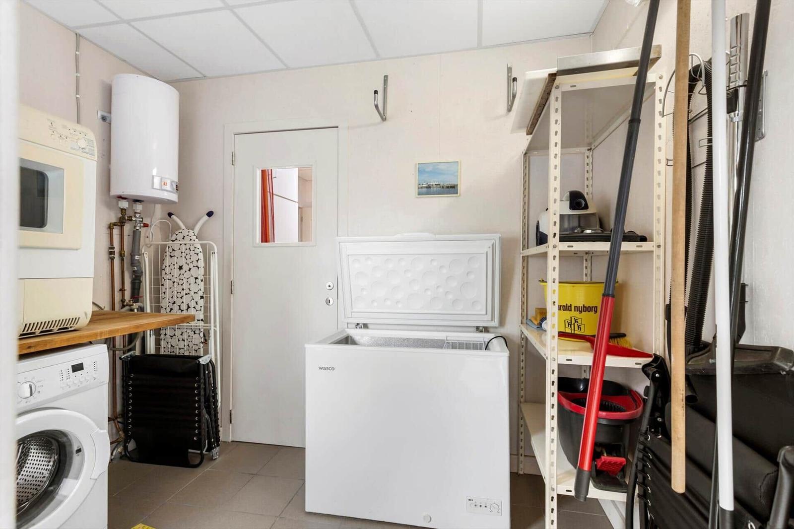 Kitchen with washing machine, freezer, and shelf with cleaning supplies.
