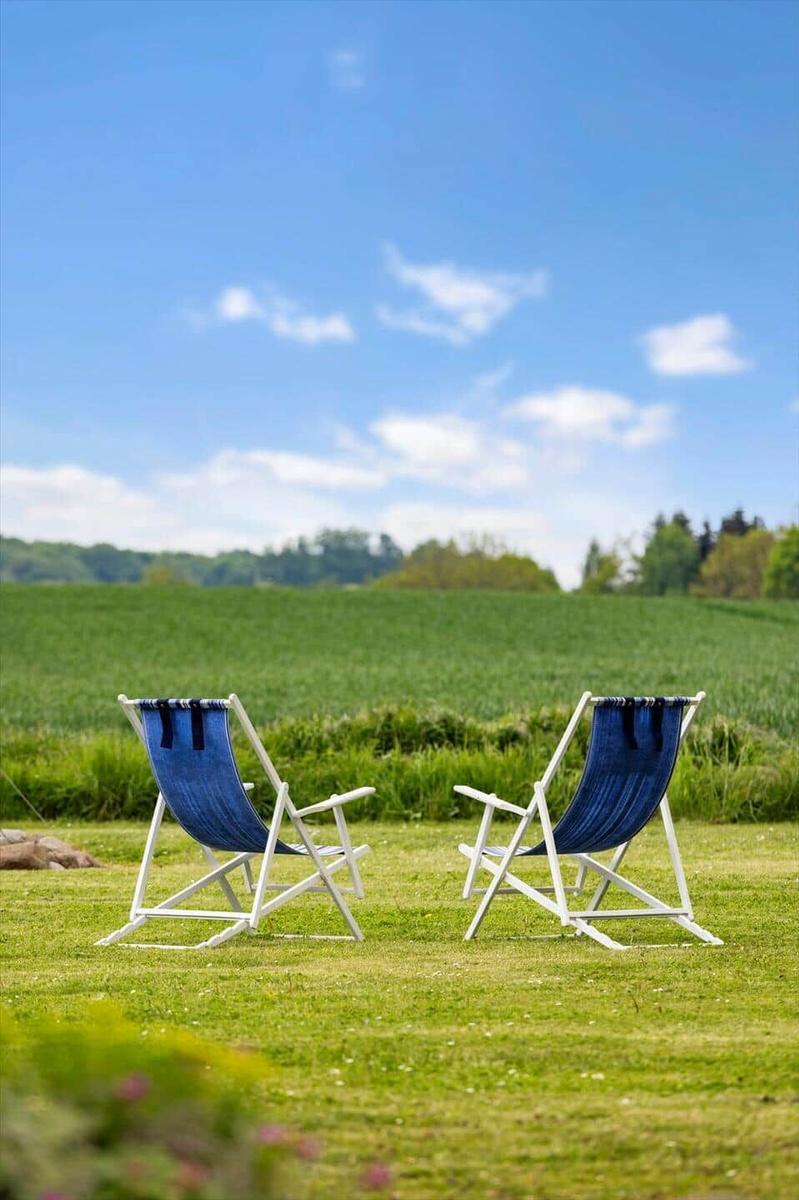 Two blue lounge chairs on a green lawn under a blue sky.