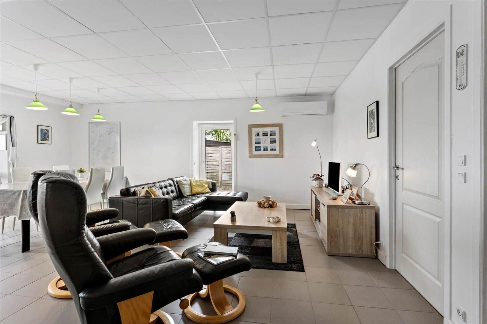 Living and dining area with black leather sofas, wooden table, and TV.