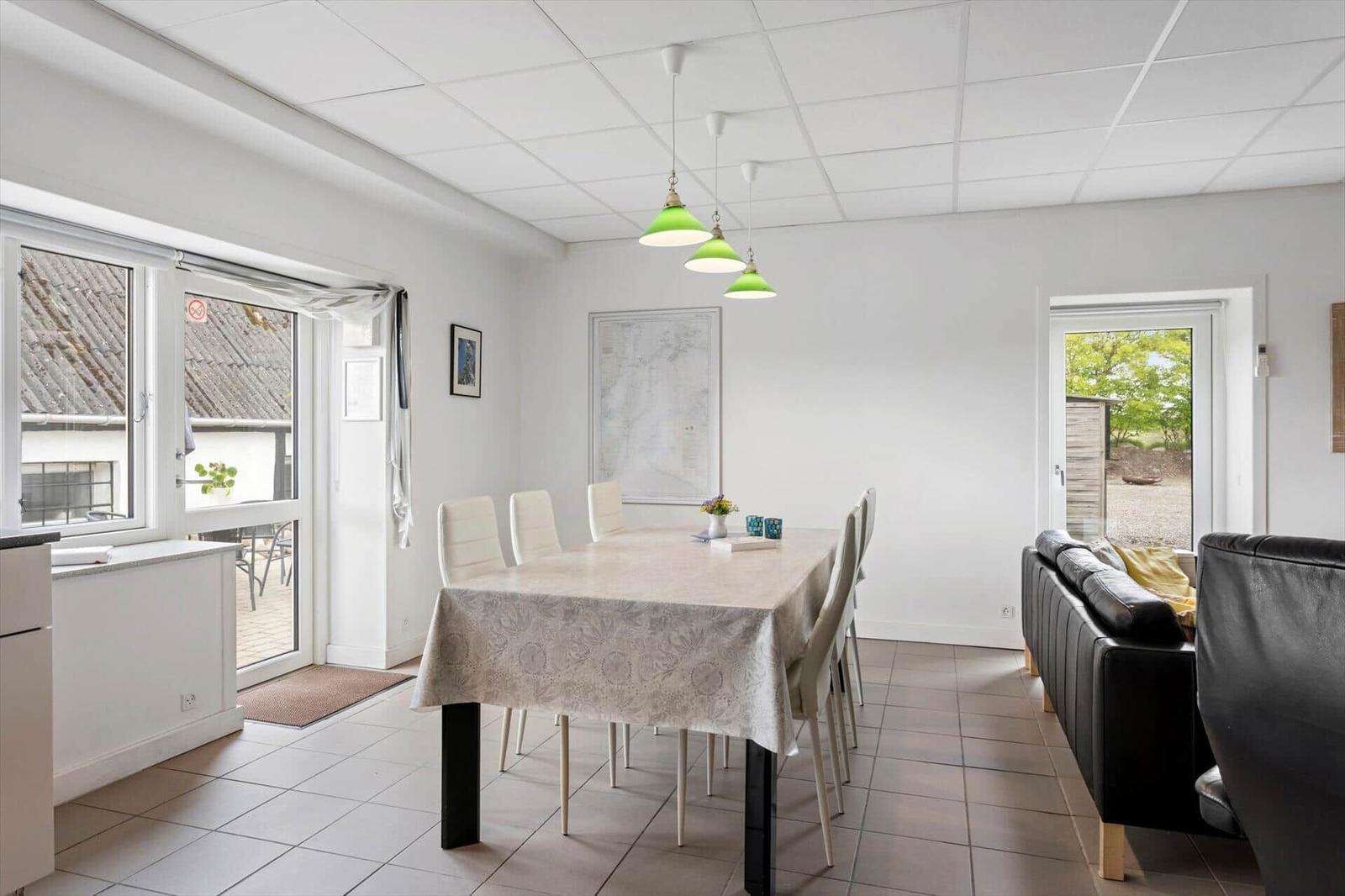 Dining room with table, chairs, and green lamps. Living area with sofa and windows.