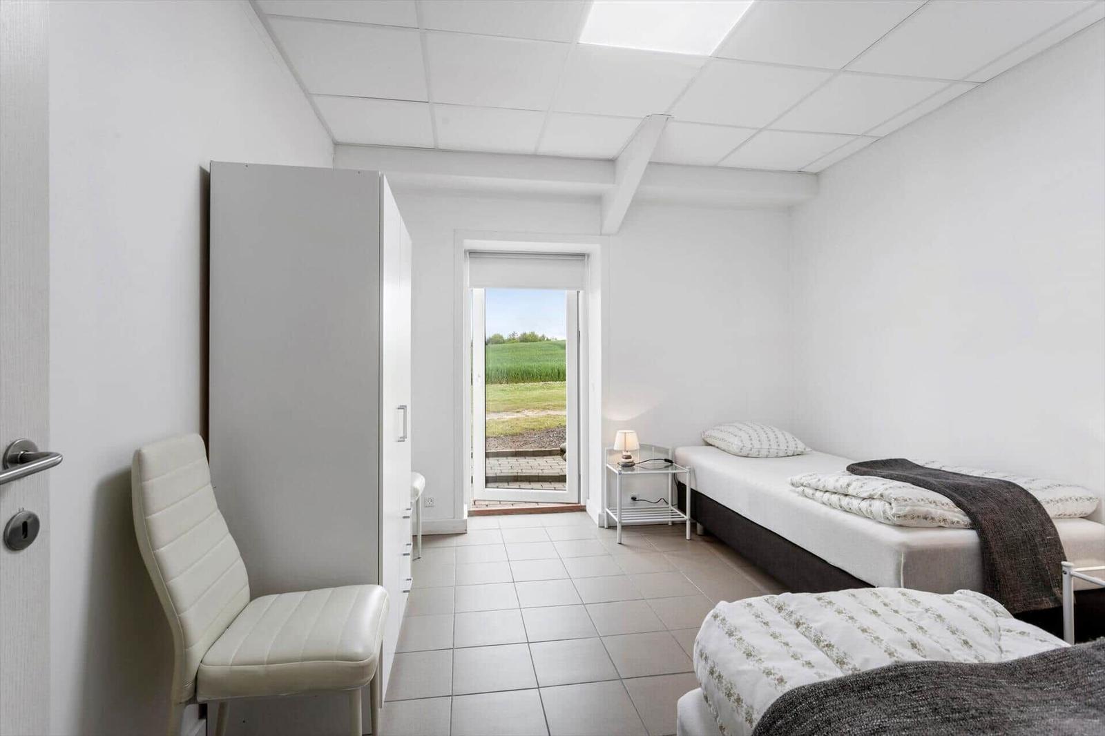 Room with two beds, wardrobe, and chair. Door leads to an outdoor area.