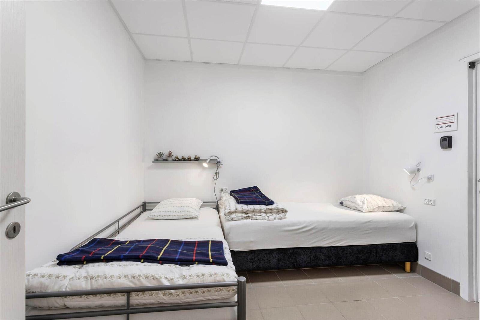 Two beds in a room with white walls and a ceiling with built-in lights.