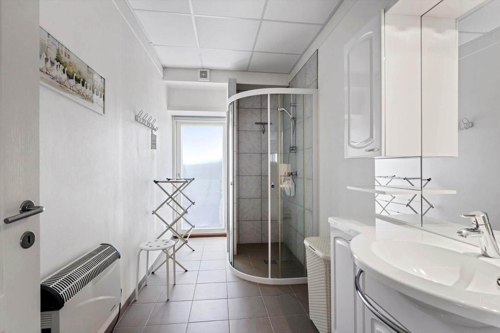 Bathroom with shower, sink, and window. White fixtures and tiles.