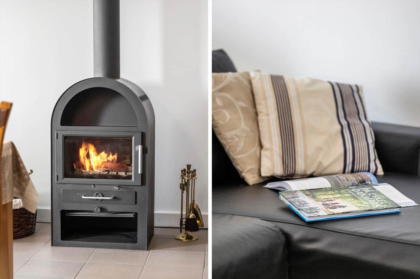 Wood stove with burning logs and sofa with cushions and book.