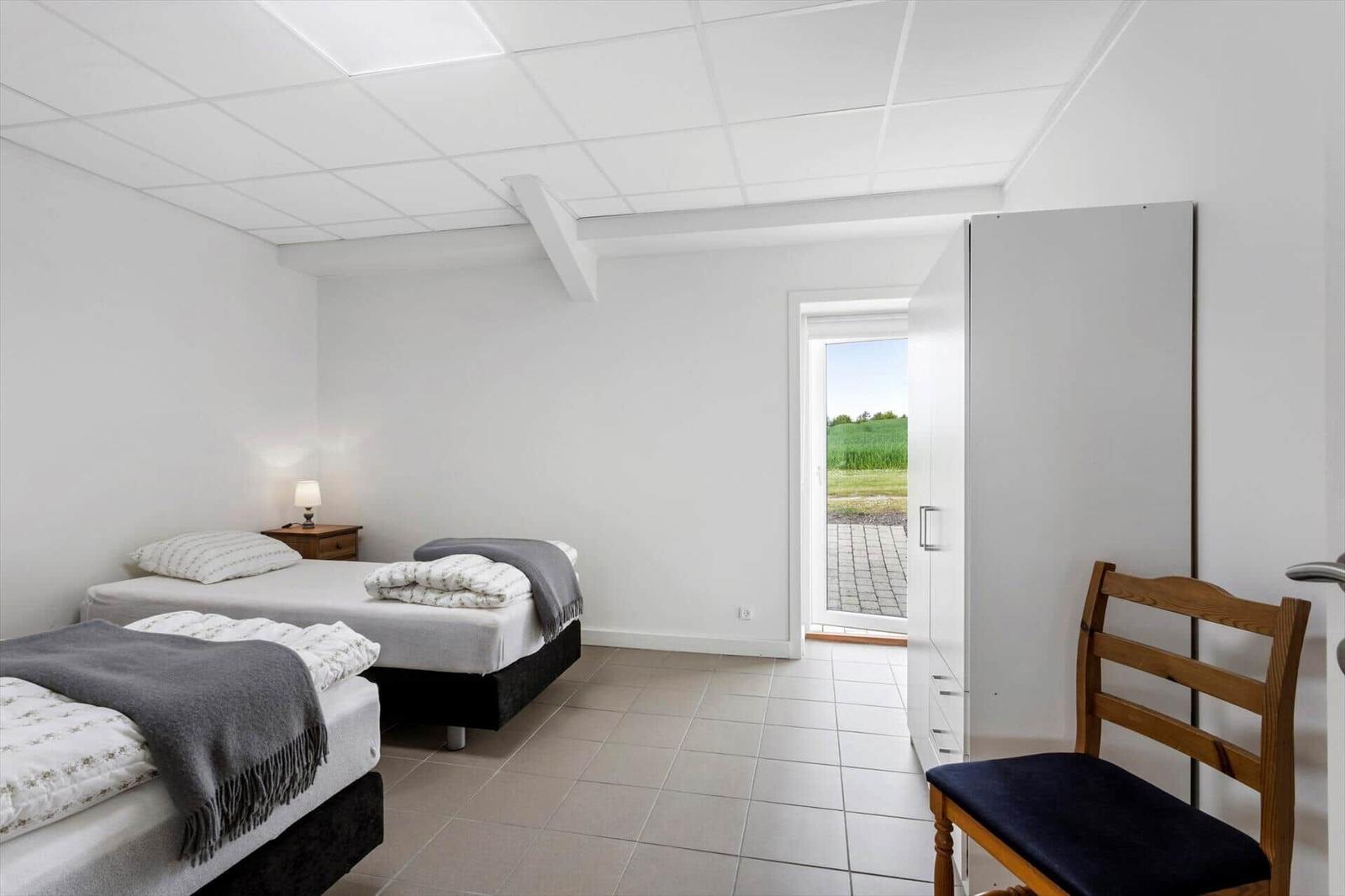 Two beds, chair, and wardrobe. Door to outdoor area with grass view.