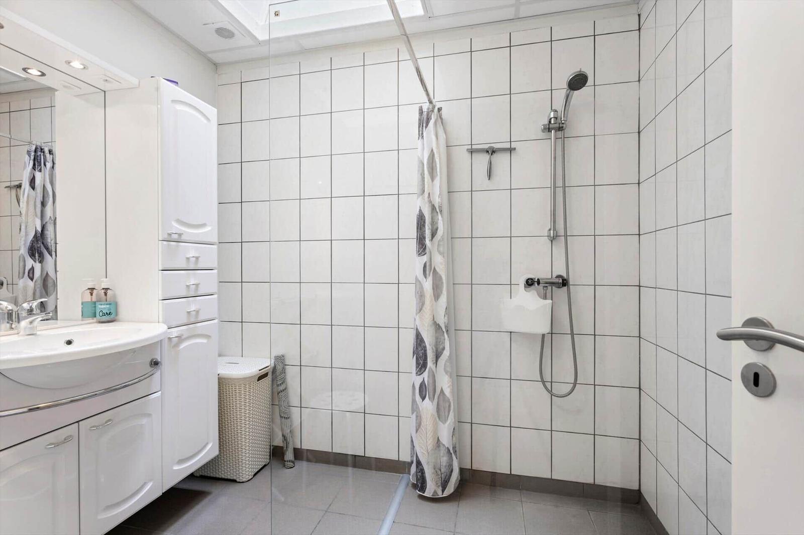 Bathroom with shower, sink, and mirror cabinet. White tiles and shower curtain.