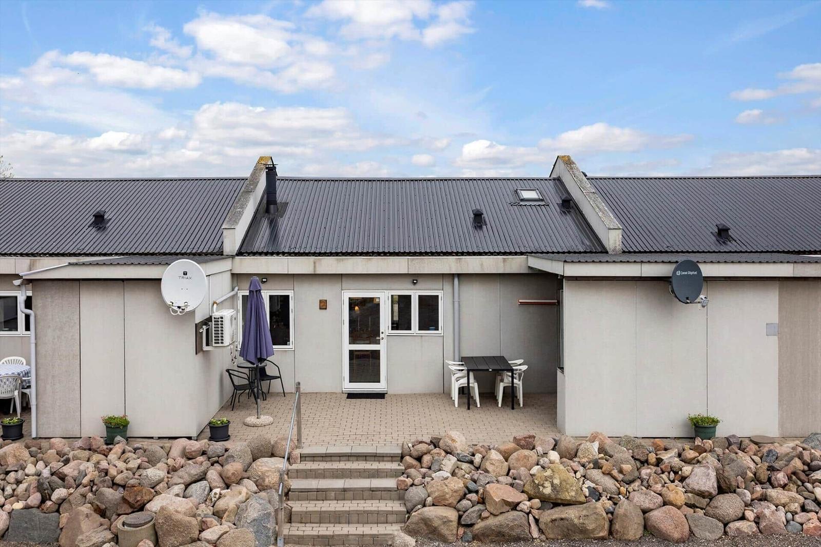 Modern vacation home with terrace, table, chairs, and satellite dishes under blue sky.