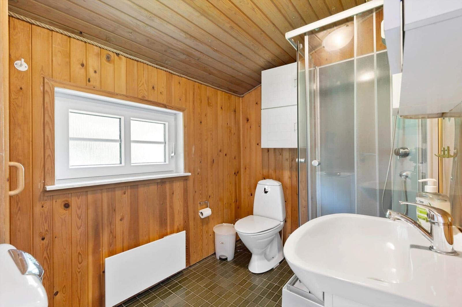 Bathroom with shower, toilet, and sink. Wooden walls and window visible.