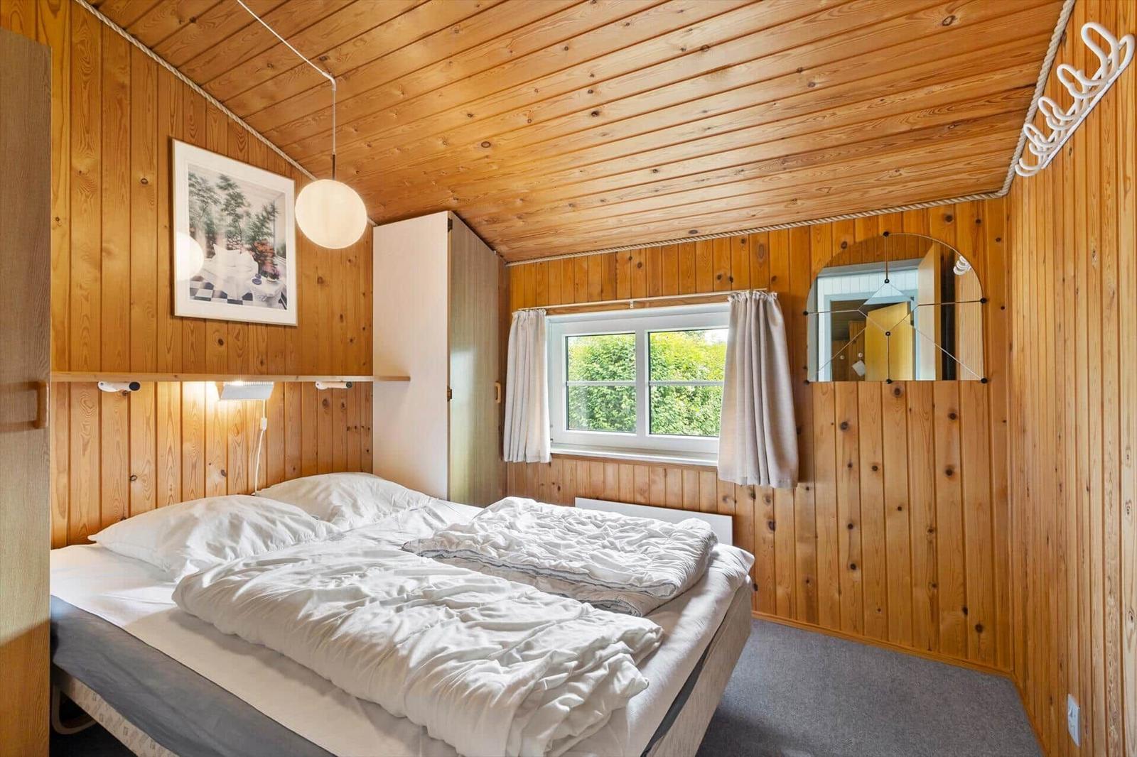 Bedroom with wooden walls, bed, and window with view of greenery.