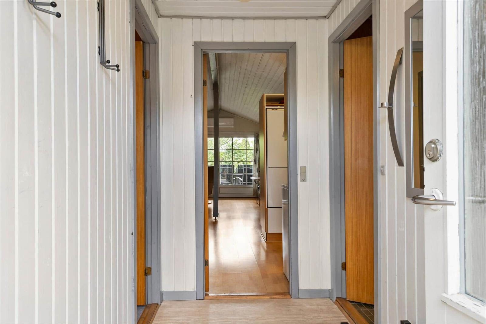 Hall house with wooden floor and white walls. Corridor to kitchen and bedroom.