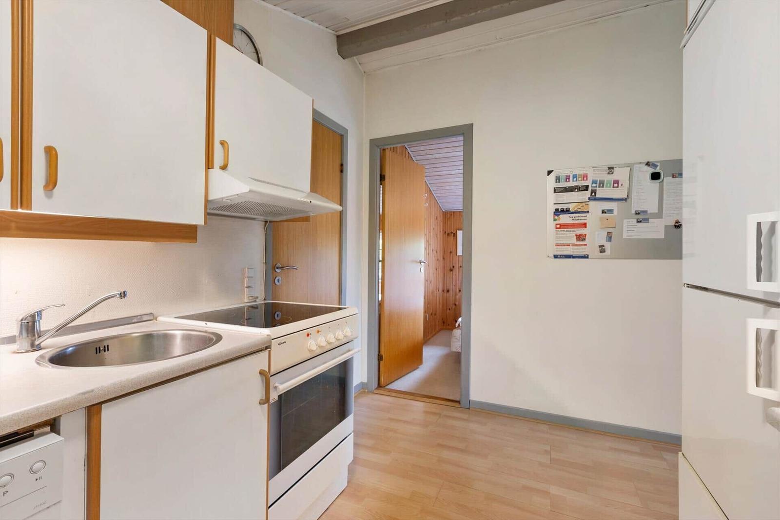 Kitchen with sink, stove, and refrigerator. Wooden floor and door to bedroom.