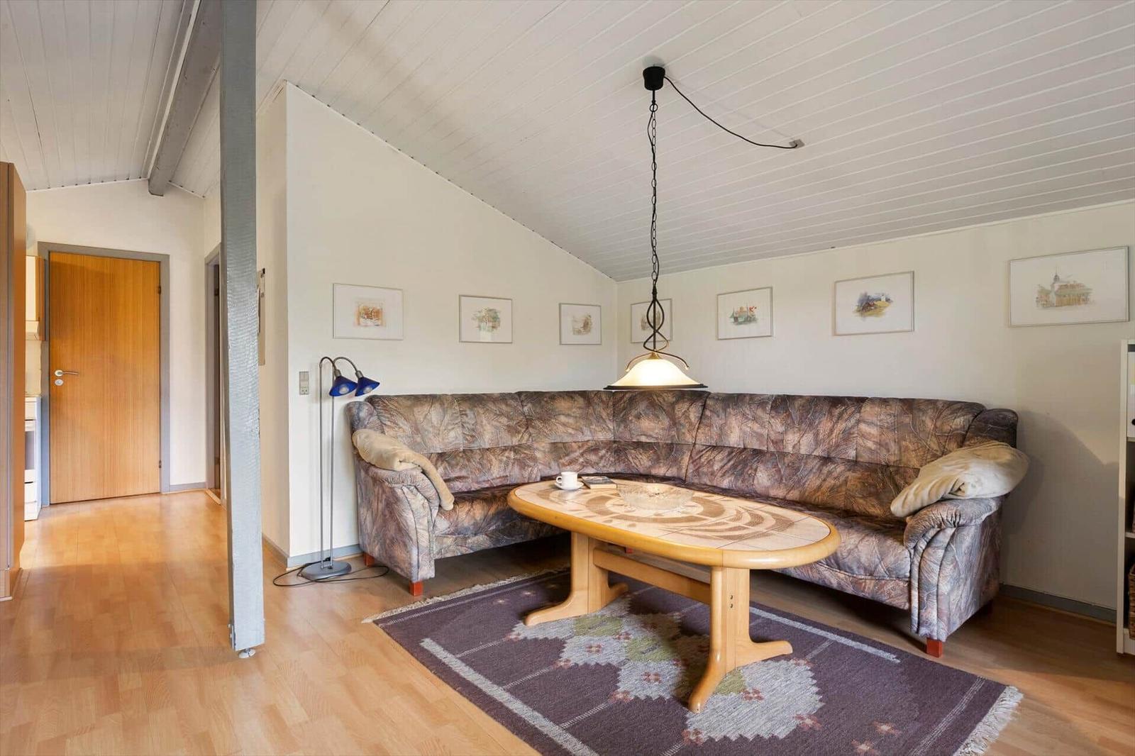 Living room with corner sofa, wooden table, and rug under sloped ceiling.