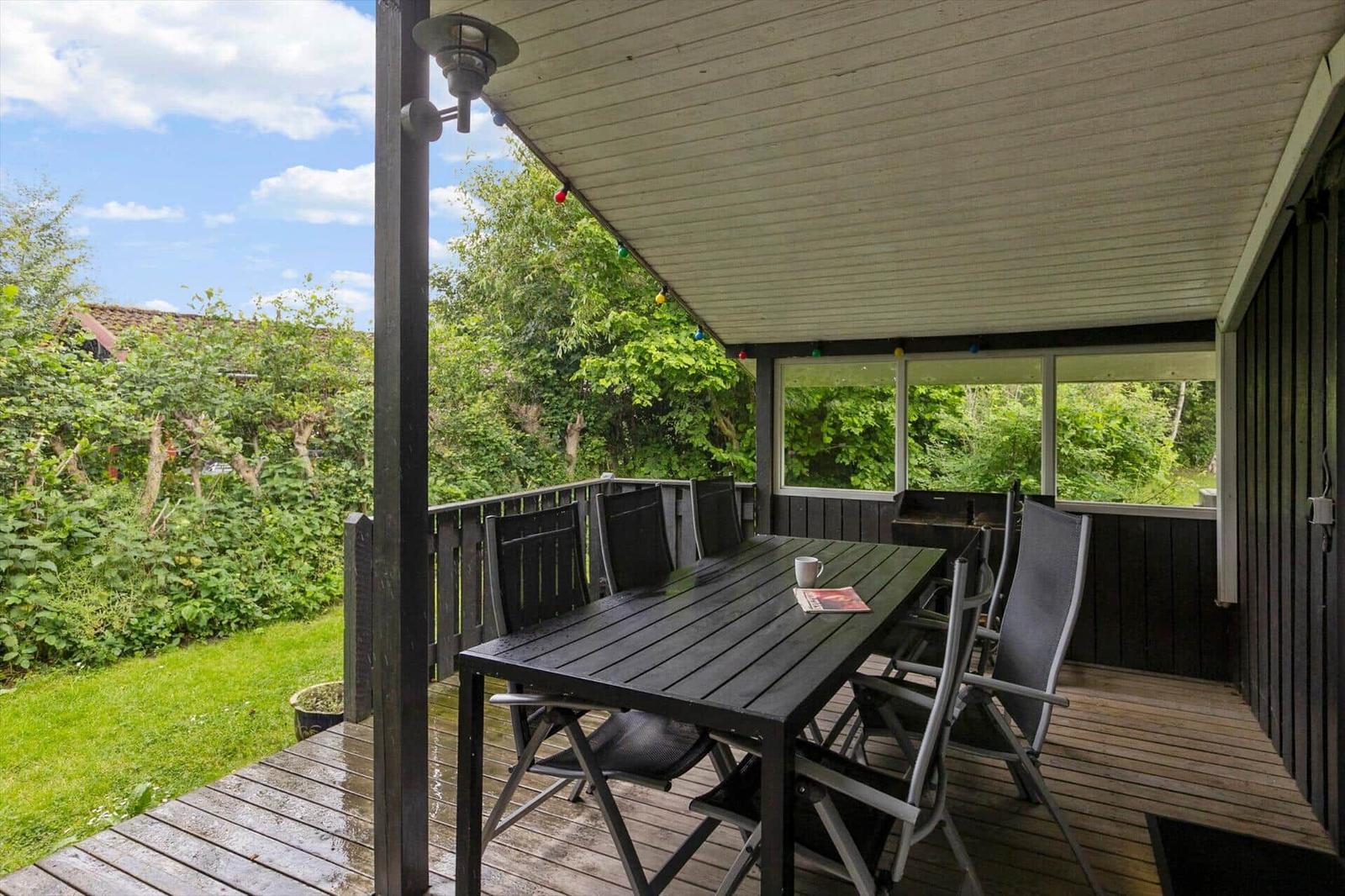 Deck with table and chairs, view of green surroundings and sky.