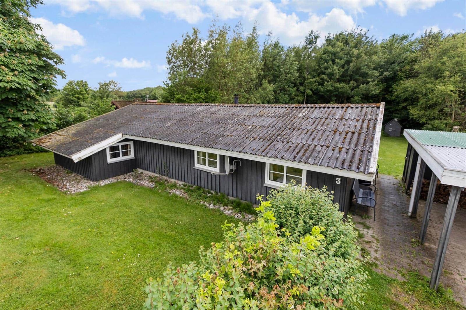 A dark-painted house with a gray roof and white window frames stands in a green setting.