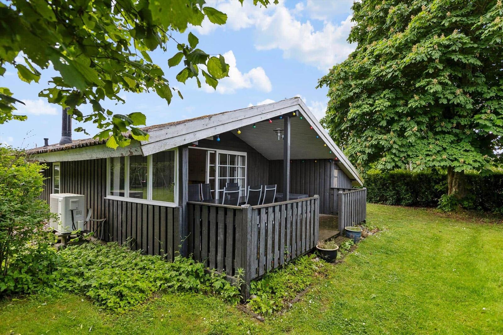 Wooden house with terrace, garden, and trees under blue sky.