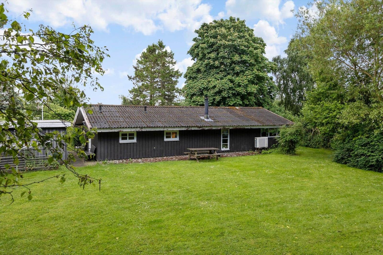 A wooden house with a garden, picnic table, and trees in the background.