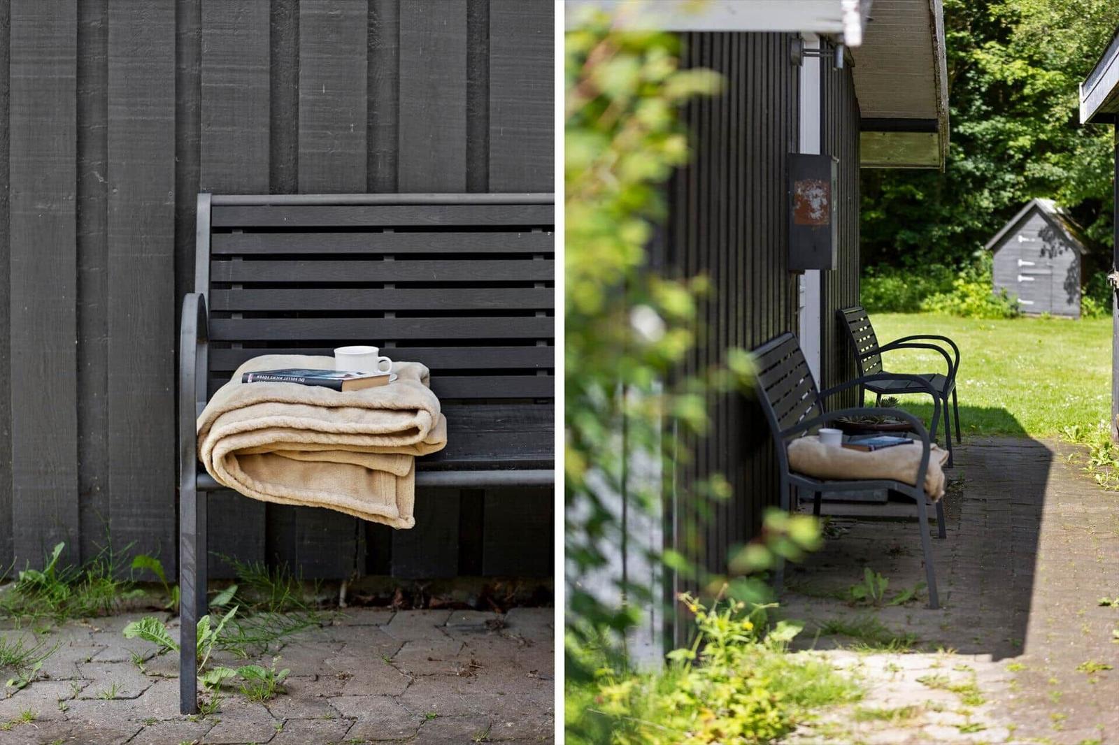 Black bench with blanket and cup against wooden wall. Outdoor seating area.