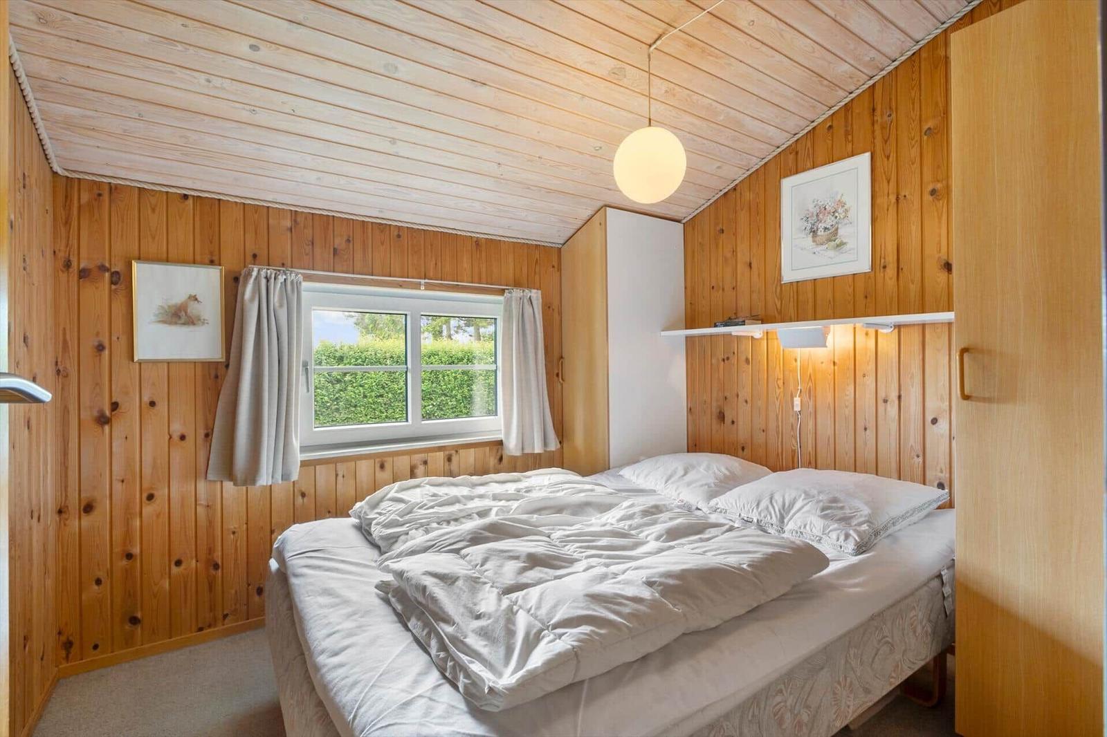 Bedroom with wooden walls, bed, and window with view of greenery.