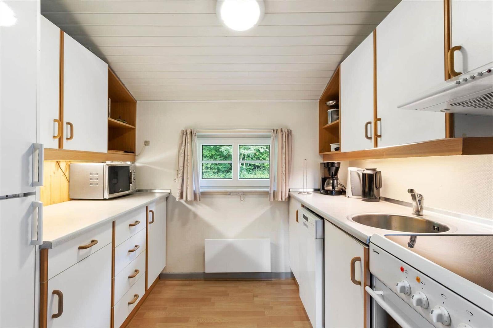 Kitchen with white cabinets, stove, sink, and window with view of greenery.