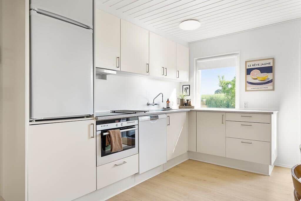 Modern kitchen with white cabinets, refrigerator, stove, and window.
