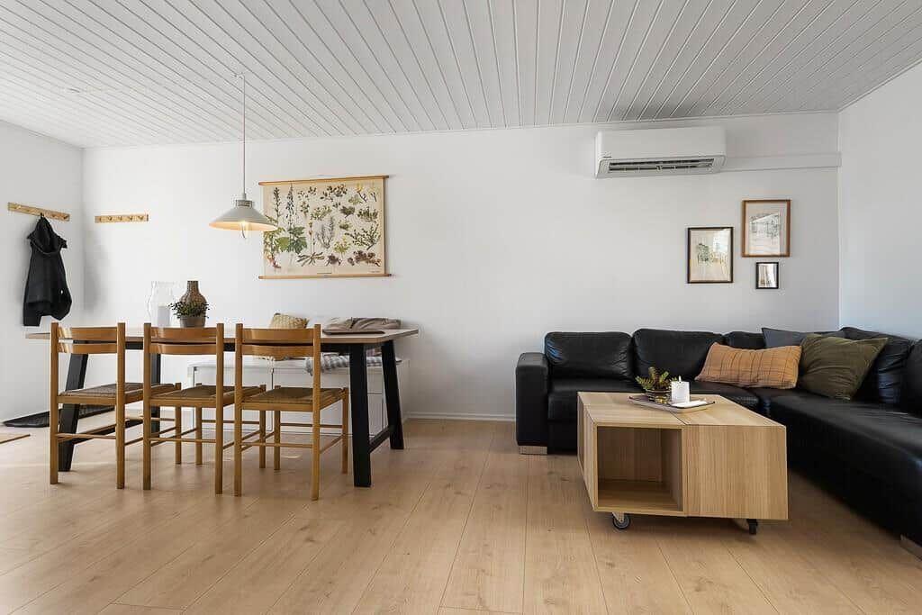 Wohn- und Essbereich mit schwarzer Couch, Holztisch und Holzfußboden.